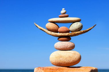 Denizin arka planındaki kumsalda renkli çakıl taşlarından oluşan bir taş zen piramidi. Yaşam dengesi, uyum ve meditasyon kavramı