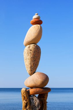 Denizin arka planındaki kumsalda renkli çakıl taşlarından oluşan bir taş zen piramidi. Yaşam dengesi, uyum ve meditasyon kavramı