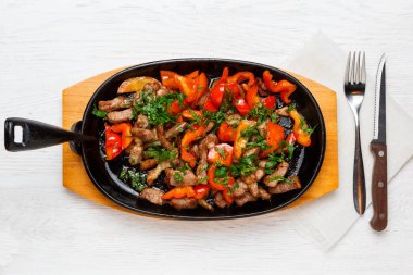 Kızarmış domuz eti, kırmızı dolmalık biber ve tavada beyaz ahşap bir masa, çatal, çatal, üst manzara.