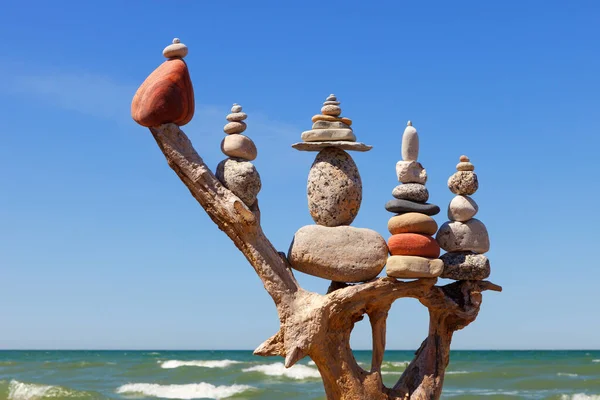 stack of multicolored balanced stones on an old wooden snags, on a blue sky and sea background. Concept of harmony and balance.
