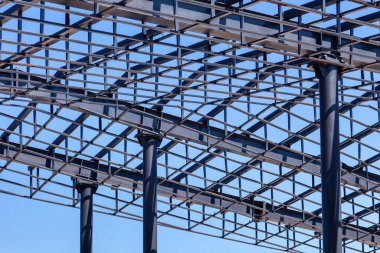Açık metal çatı çerçevesi mavi gökyüzü arka planına karşı metal sütunlar tarafından destekleniyor