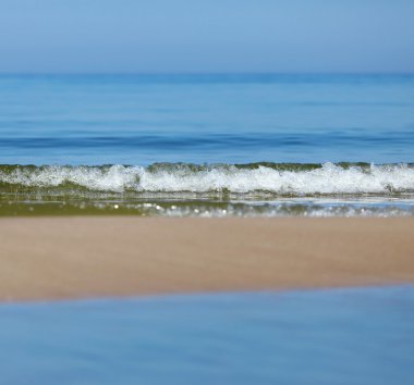 Deniz sakin, gökyüzü ve kum şeridi.