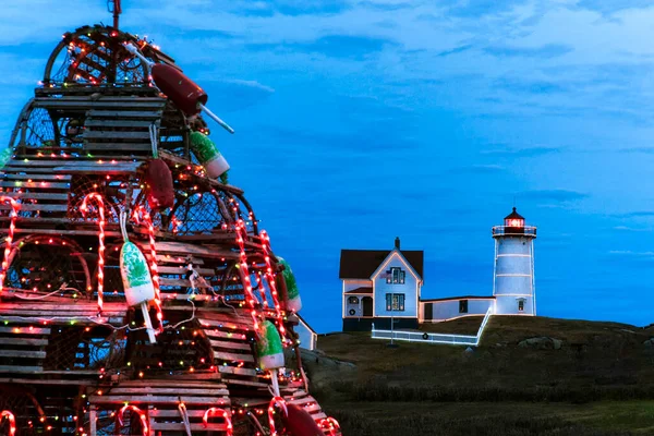 メイン州の休日にはヌブル灯台がライトアップされ 前景には伝統的な木製のロブスタートラップホリデーツリーがあります ニューイングランドの伝統 ロイヤリティフリーのストック画像