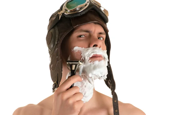 man shaving with shaving foam on his face in a flight helmet and flying goggles arrogantly looking at camera