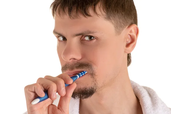 serious adult man with white towel on his shoulders looking at camera and cleaning teeth