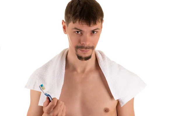 male with white towel on his shoulders looking at camera and holding in his hand white and blue toothbrush