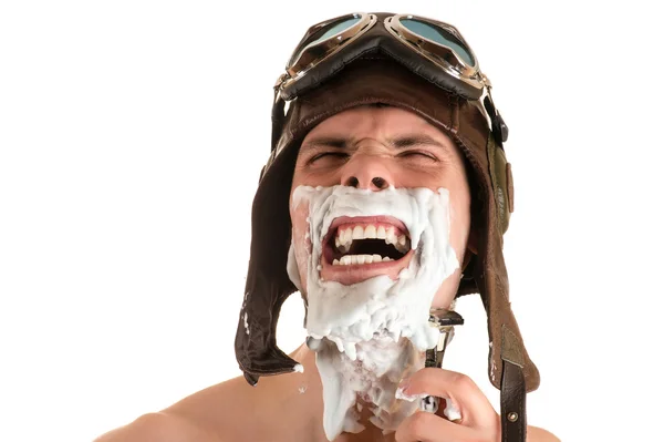 screaming man shaving with shaving foam on his face in flight helmet and flying goggles