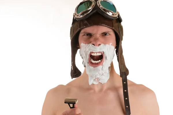 Hombre gritando con espuma de afeitar en su cara en casco de vuelo y gafas voladoras con afeitadora Imágenes de stock libres de derechos