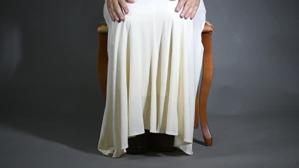 Чоловік у білій сукні сидить на стільці тягне сукню і показує старе взуття — стокове відео