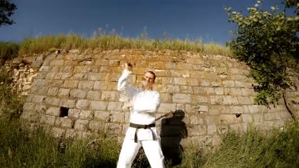 Homem de kimono branco treina com nunchaku com rosto sério — Vídeo de Stock