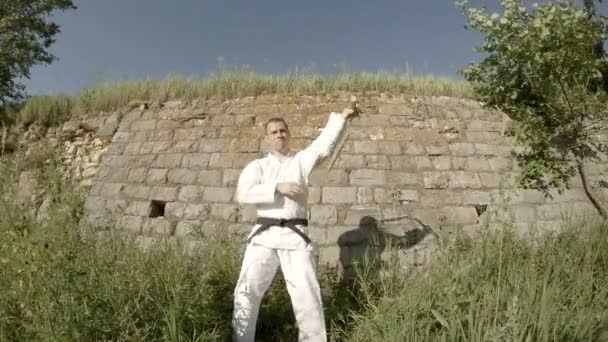 Человек в белом кимоно тренируется с нунчаку — стоковое видео
