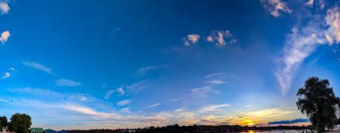 Nehre parlak altın, sarı ve mavi renkli dramatik bir günbatımı yansıdı. Kıyıdaki ormanın kenarı gökyüzünü ve suyu ayırır. Sıcak ve serin tonların göksel etkileşiminin nefes kesici bir resmi..