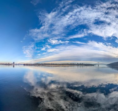 Bulutlar nehre yansıyor. Suyun yüzeyinde buhar kabarcıkları uçuşuyor. Gökyüzü ve dalgalarla dolu bir manzara. Tatlı su rezervleri. Büyük yansıma hacmi ayna yüzeyi. Gün mavi soğuk gökyüzü.
