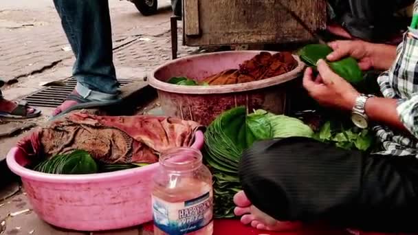 Il vecchio è seduto sul lungomare mentre prepara le foglie di betel per i negozi . — Video Stock