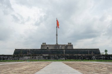 Antik bir Vietnam İmparatorluk Kalesi 'nin heybetli taş duvarları ulusal bayrağın heybetli bir şekilde dalgalandığı dramatik bulutlu gökyüzüne karşı tarihi bir ihtişam sergiliyor..