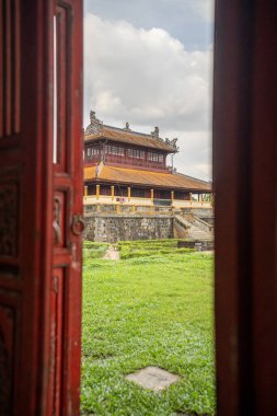 Görkemli bir Vietnam İmparatorluk Sarayı 'nın süslü kırmızı ahşap kapısından, yemyeşil bahçeler ve gökyüzünün altındaki antik mimariyle çevrili.