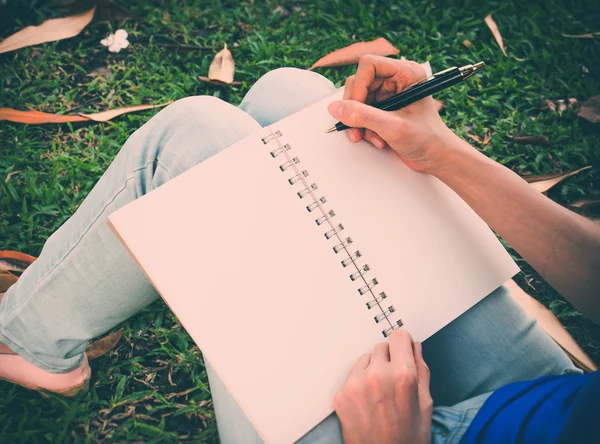 Giovane donna seduta nel parco che scrive qualcosa nel libro — Foto Stock