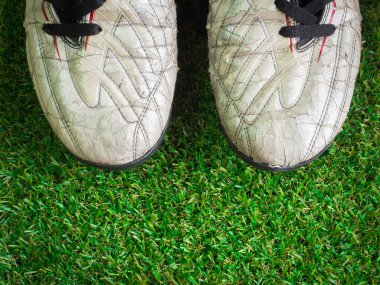 Suni çim üzerinde eski çamurlu kirli futbol ayakkabıları 
