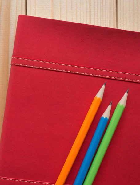 Matite colorate messe su diario rosso sulla scrivania di legno — Foto Stock