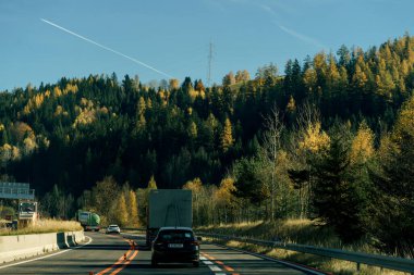 Avusturya, 10.29.2025 Avusturya Alpleri 'ndeki bir sonbahar ormanının arka planında trafik vardı. Arabayla tatil gezisi. Mevsimlik taşıma sahnesi.