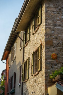 Yıllanmış kepenkler ve parlak gün ışığı altında sıcacık parlayan dekoratif bir güneş yüzüyle süslenmiş taşralı bir İtalyan taş binası.
