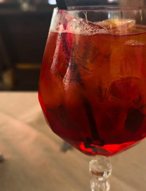 Bardakta Aperol Spritz kokteyli, buz küpleri ve restorandaki bir masada siyah bir pipet. Kokteyl Negroni