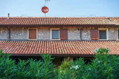 Terracotta çatı kiremitleri, ahşap panjurları ve İtalya 'da açık mavi gökyüzünün altındaki bahçe bitkileriyle geleneksel taş ev.