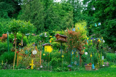 Kuş evleri, çiçekler ve el yapımı süslemeleri olan parlak yaratıcı bir bahçe. Serin bir arka bahçede yemyeşil ve canlı renkler..