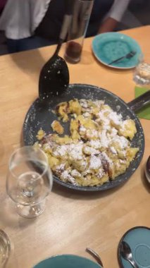 Geleneksel Avusturya tatlıları Kaiserschmarrn masaya servis ediliyor ve üzerine pudra şekeri serpiştiriliyor. Otantik Alp mutfağı ve rahat restoran sahnesi.