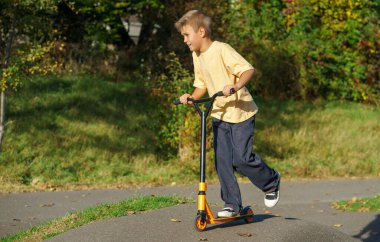 Sunny Park 'ta asfalt pompa pistinde scooter süren aktif bir çocuk. Sağlıklı açık hava yaşam tarzı, çocukluk eğlencesi, spor aktivitesi ve özgürlük kavramı