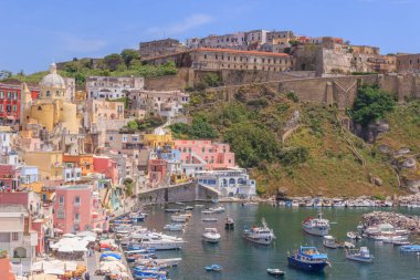 Güneşli yaz gününde güzel Procida 'nın panoramik manzarası. Marina Corricella 'daki renkli evler, kafeler ve restoranlar, balıkçı tekneleri ve yatlar, Procida Adası' ndaki açık mavi gökyüzü ve masmavi deniz. İtalya 'nın 2022 Kültür Başkenti olarak taçlandırıldı..