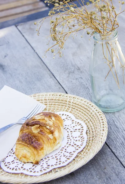 Almond croissant op houten tafel en droge bloem in glazen fles — Stockfoto