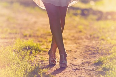 gün batımına doğru toprak yolda yürüyen genç kadın bacakları.