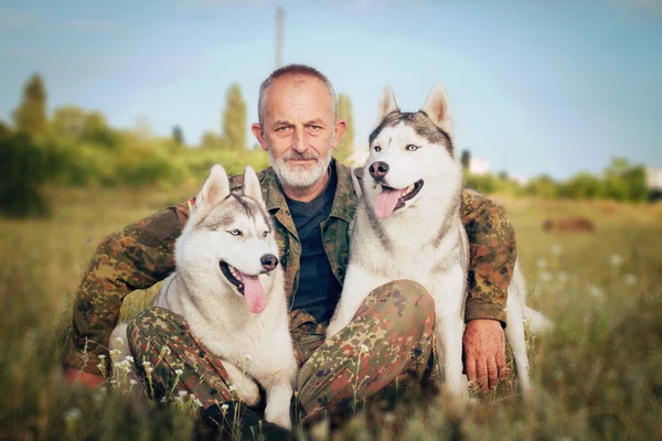 Viejo con barba sentado en un pajar con sus perros, disfrutando del atardecer de verano. Husky siberiano —  Fotos de Stock