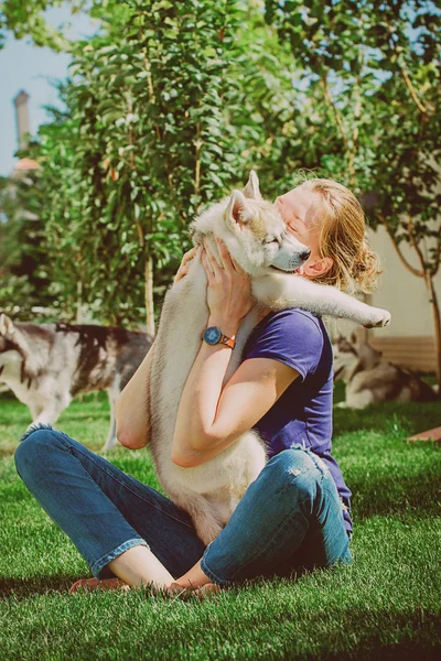 Молодая девушка играет с собакой. Щенок сибирского хаски. Женщина с улыбающейся собакой сибирского хаски, сидящая в солнечный день, на прогулке с собакой . — стоковое фото