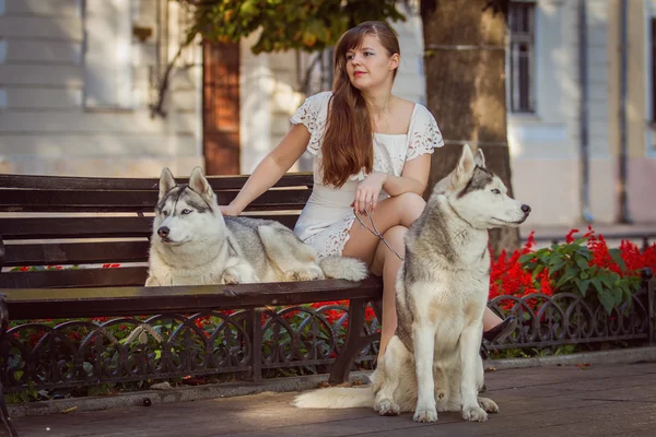 Chica caminando por la calle con dos perros. Una chica con un vestido blanco. Huskies siberianos . —  Fotos de Stock