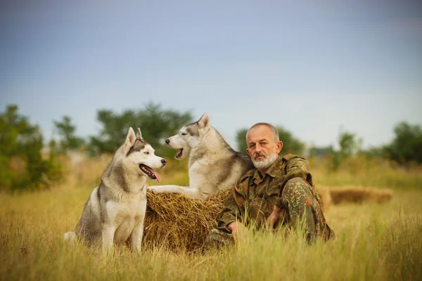 Viejo con barba sentado en un pajar con sus perros, disfrutando del atardecer de verano . —  Fotos de Stock