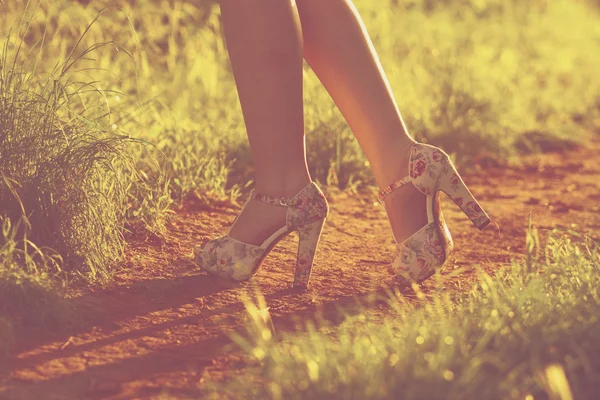 Young female legs walking towards the sunset on a dirt road.