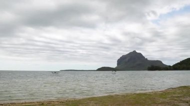 Denizden yükselen görkemli bir dağın olduğu kasvetli bir gökyüzünün altında dramatik bir sahil şeridi ve küçük bir deniz uçağı zarif bir şekilde suyun üzerinde süzülüyor..