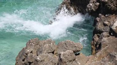 Bozulmamış bir tropikal kıyı şeridinin yüksek açılı görüntüsü. Parlak turkuaz suların, el değmemiş sahil şeridinin dayanıklı, güneşli kaya oluşumlarına karşı köpüklü bir dansa dönüşmesi..