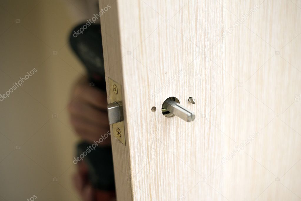 Installation of door lock using a screwdriver to. Carpenter at lock installation with electric drill into wood door