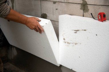 Bir müteahhit polistiren köpük çarşaf takar. Evin duvarlarının termal izolasyon süreci. Termal yalıtım.