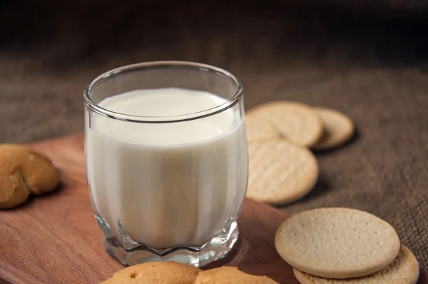 Un verre de lait avec des biscuits sur une planche de bois sur un sac de fond, toile de jute , — Photo