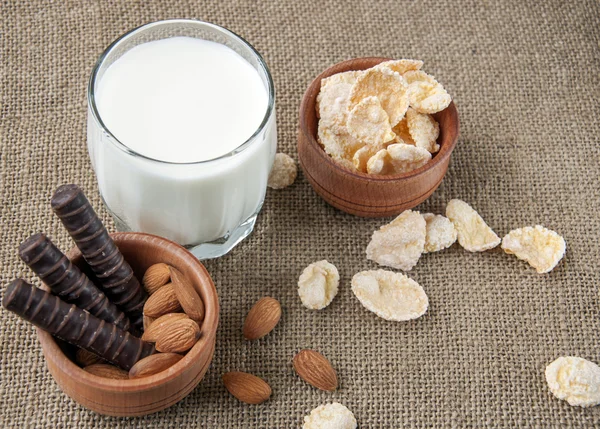 Ein Glas Milch mit Mandelnüssen, Cornflakes, Pralinen, auf einem Hintergrund Verpackung, Klette, — Stockfoto