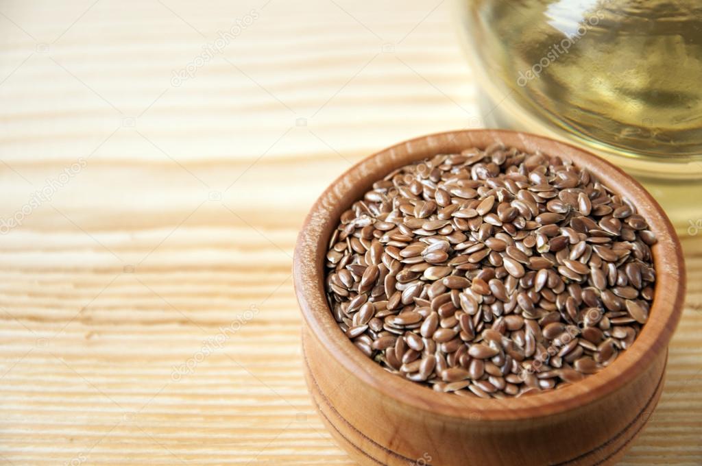 Flax seeds in a wooden bowl and linseed oil on a wooden background