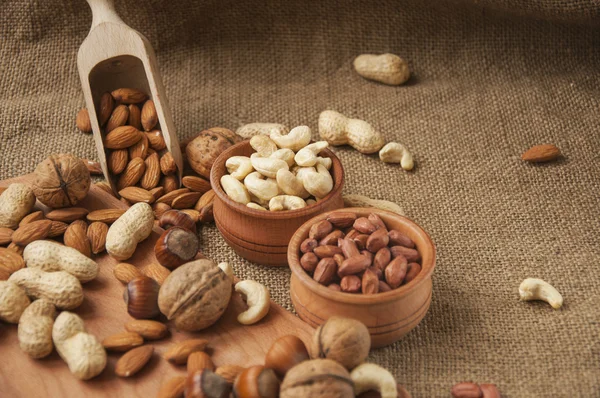 Almendras, anacardos y avellanas en cuencos de madera sobre fondo de madera y arpillera — Foto de Stock