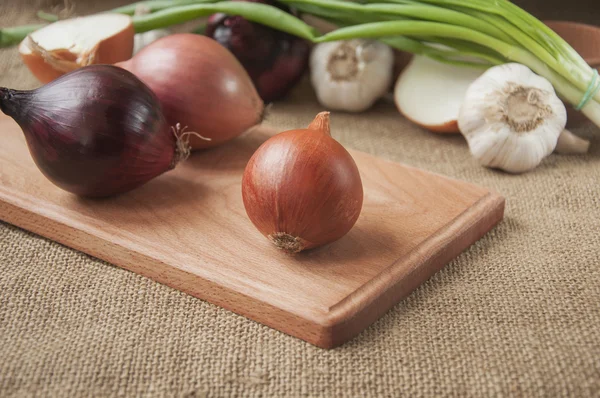 Various onions on a board on a background sacking, burlap — Stock Photo, Image