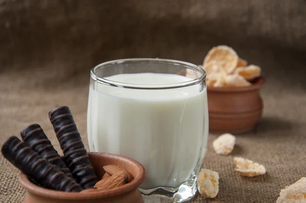 Ein Glas Milch mit Mandelnüssen, Cornflakes, Pralinen, auf Kleckerhintergründen — Stockfoto