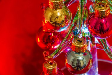Camdan yapılmış küçük bir Noel ağacının süsleri. Yandan bakıldığında kırmızı arka planda. Boşluğu kopyala.