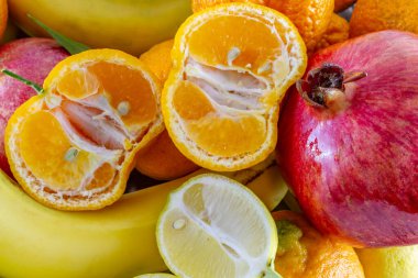 Muz, nar, dilimlenmiş limon ve dilimlenmiş mandalinadan oluşan çeşitli taze meyve düzenlemeleri..